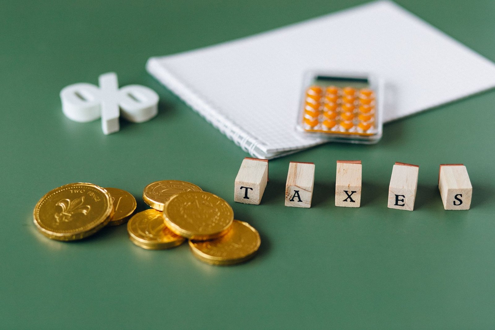 Close-up of tax-related items including coins, calculator, and word 'taxes' on a green background.