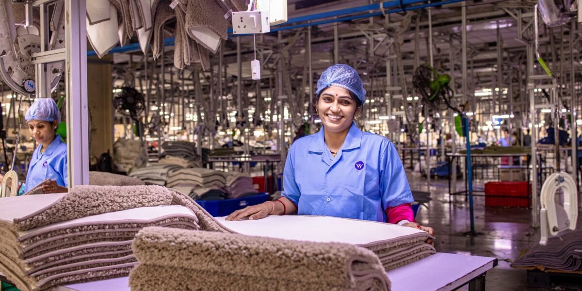 A smiling female worker in a textile factory, handling fabric with care.